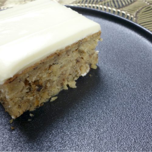Banana nut slice with lemon cream cheese frosting served on a black plate.